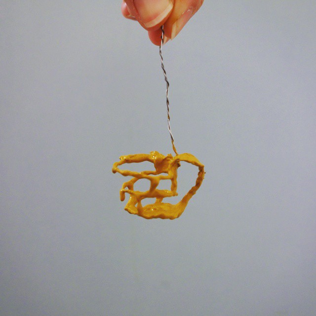 66: Tiny hanging three-dimensional sculpture of a teacup made with acrylic paint dripped over a wire frame